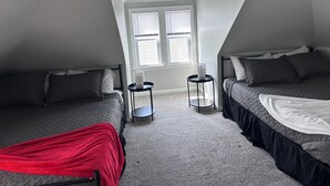 A bedroom with two beds, a window, and a ceiling light fixture.