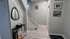 A hallway with a staircase, a mirror, and framed pictures on the wall.