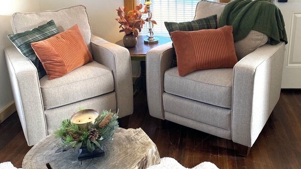 Una sala de estar acogedora con dos sillones, una pequeña mesa de madera con una vela y una ventana con persianas.