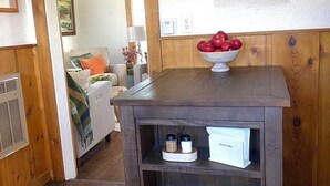 Una mesa de madera con un bol de manzanas y un portavasos en una habitación con paredes de madera y una puerta que da a otra estancia.