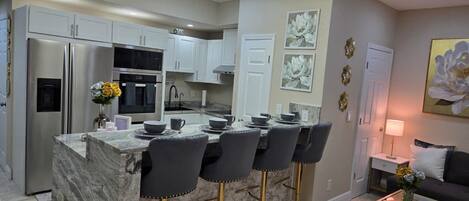 A modern kitchen with a central island, bar stools, and a dining area with a sofa and coffee table.