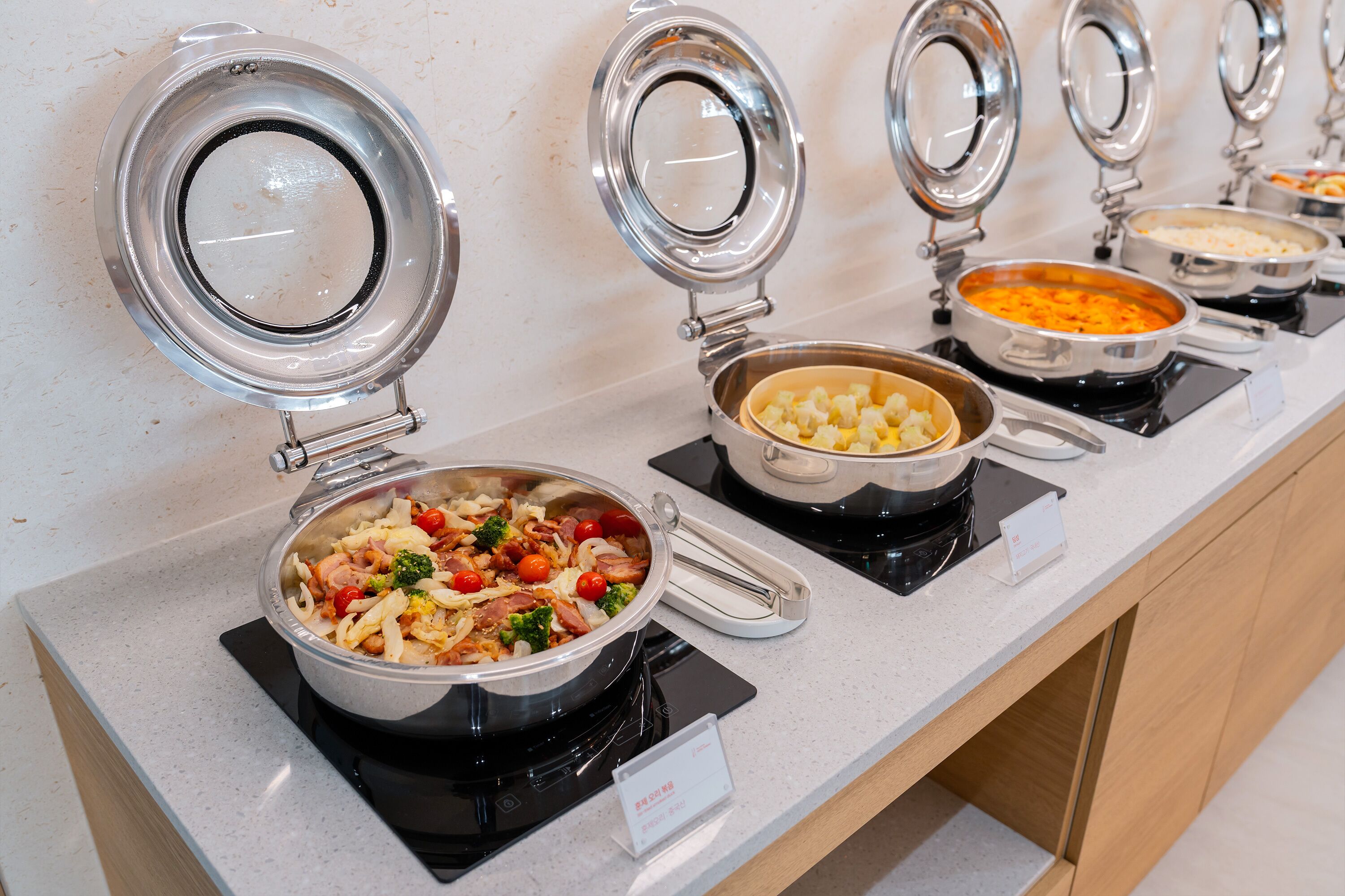 A buffet setup with various dishes in metal containers, a salad with vegetables and meat, and a sign indicating the type of cuisine.