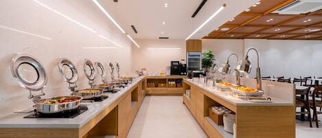 Un moderno montaje tipo bufé con varias estaciones de servicio, una máquina de café y una zona de estar con sillas.