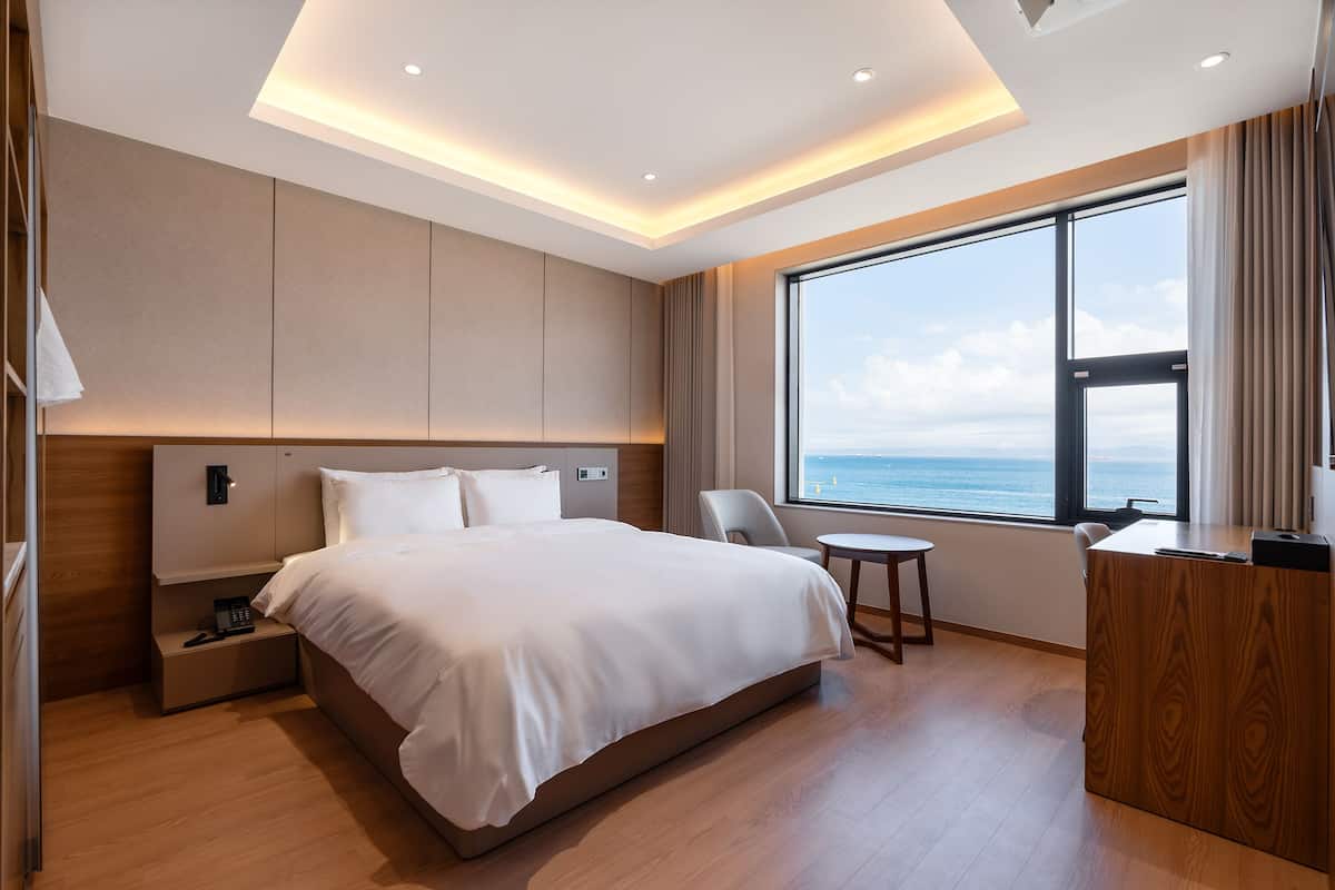 Une chambre d’hôtel moderne avec un grand lit, un bureau, une chaise et une vue sur la mer.