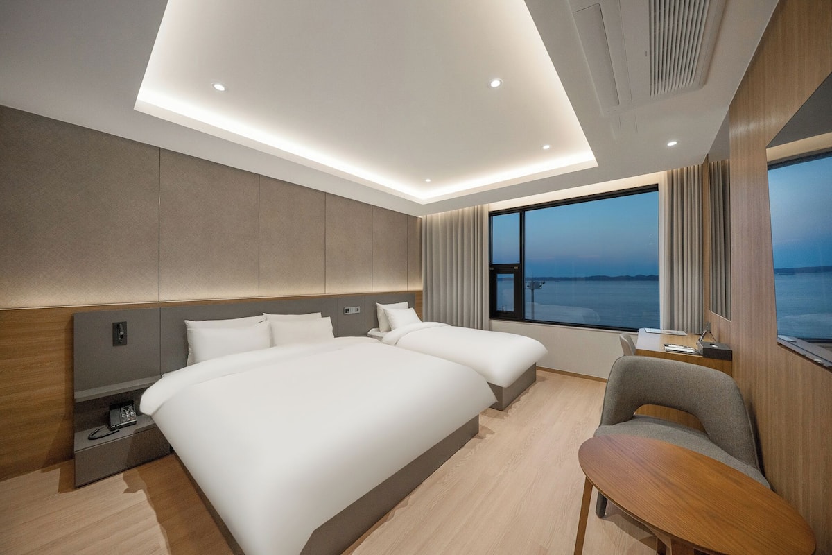 Une chambre d’hôtel moderne avec deux lits, un bureau et une vue sur la mer.