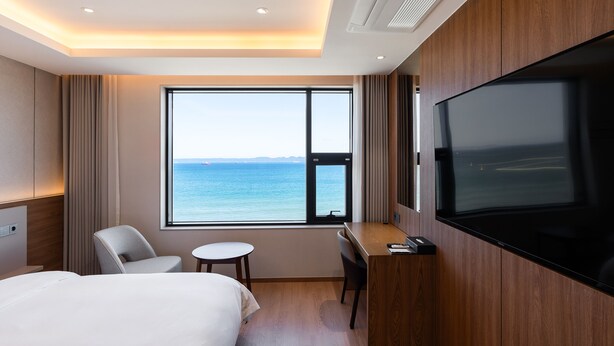 Un cuarto de hotel con una cama grande, un escritorio, una silla, un televisor y una ventana con vista al mar.