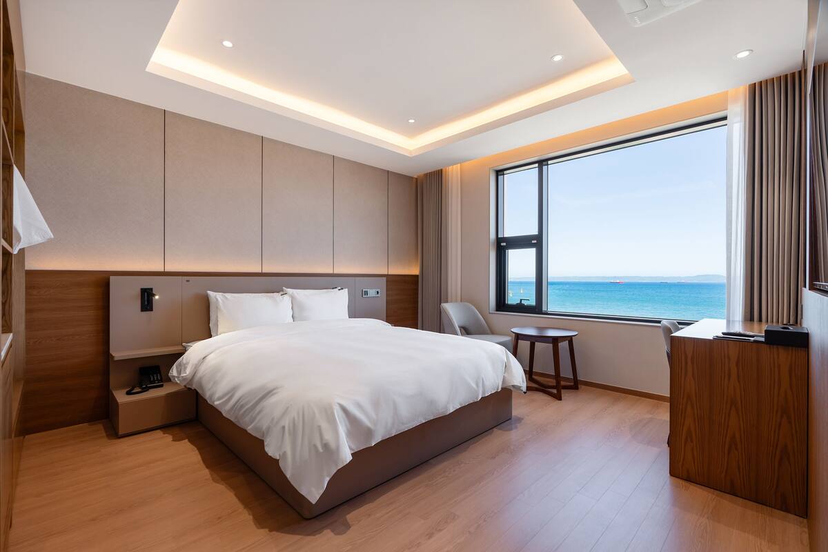Une chambre d’hôtel moderne, dotée d’un grand lit, d’un bureau et offrant une vue sur la mer.