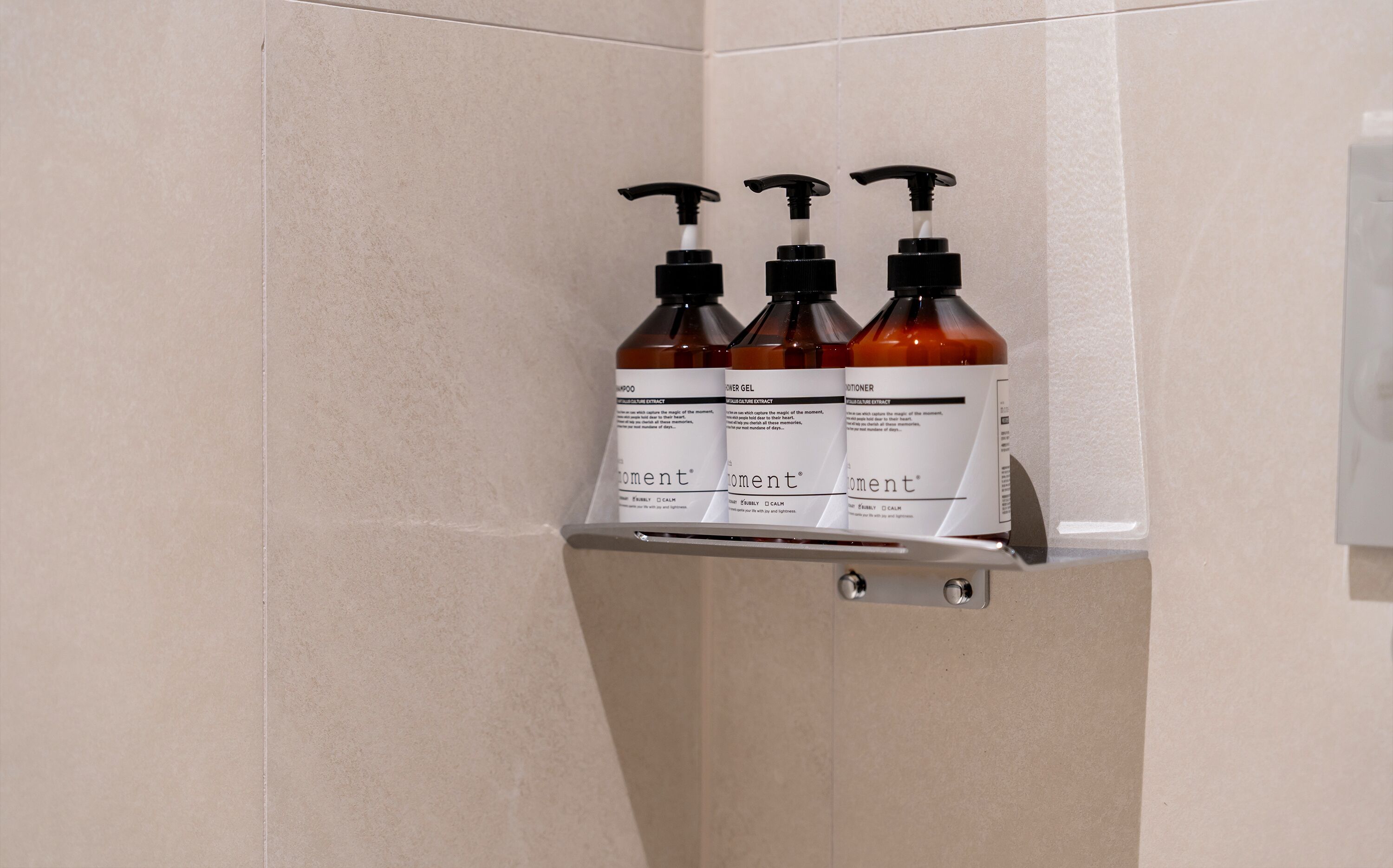 Une étagère de salle de bain avec trois flacons de produits pour les soins capillaires de la marque Moment.