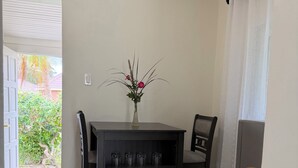 Un coin repas comprenant une table, des chaises, un vase avec des fleurs et une étagère avec des tasses.