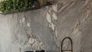 A kitchen with a marble backsplash, a gold faucet, and a coffee maker.