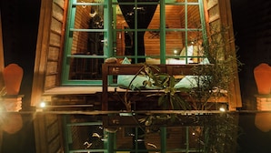 A wooden cabin with a glass facade, a visible bed, and a reflection in the water in front. - Waras Villa (Gili Trawangan)