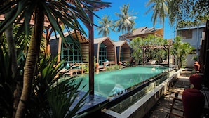 A pool area with lounge chairs, palm trees, and wooden buildings. - Waras Villa (Gili Trawangan)