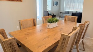 Un coin repas avec une table en bois, six chaises en osier, une plante en pot et un tableau accroché au mur.