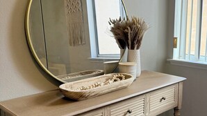 Une coiffeuse en bois, ornée d’un miroir rond, d’un bol et d’un vase contenant des fleurs séchées.