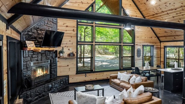 Ein gemütliches Blockhaus-Interieur mit Kamin aus Stein, Ledersofas und großen Fenstern mit Blick ins Freie.