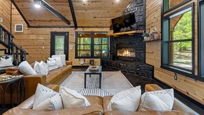 Ein gemütliches Blockhaus-Interieur mit Kamin aus Stein, Holzwänden und großen Fenstern.