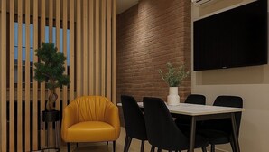 Un comedor moderno con un separador de madera, un sillón amarillo, sillas negras, una mesa y un televisor de pantalla plana montado en la pared.