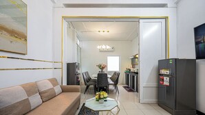 A modern living room with a sofa, a dining table with chairs, a kitchen area with a refrigerator, and a hallway leading to another room. - Saigon Central Group Stay  (Ho Chi Minh City)