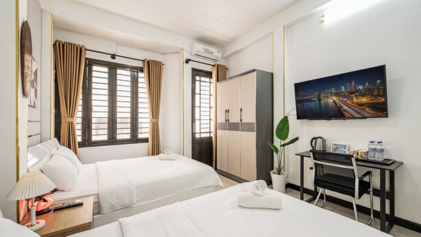 A hotel room with two beds, a desk, a TV, and a large window with curtains. - Saigon Central Group Stay  (Ho Chi Minh City)