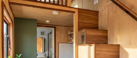 A compact kitchen with wooden cabinetry, a dining area with stools, and a staircase.