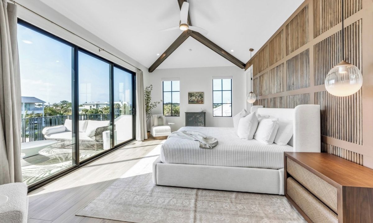 A modern bedroom with a large bed, a wooden accent wall, and a view of the outdoors.