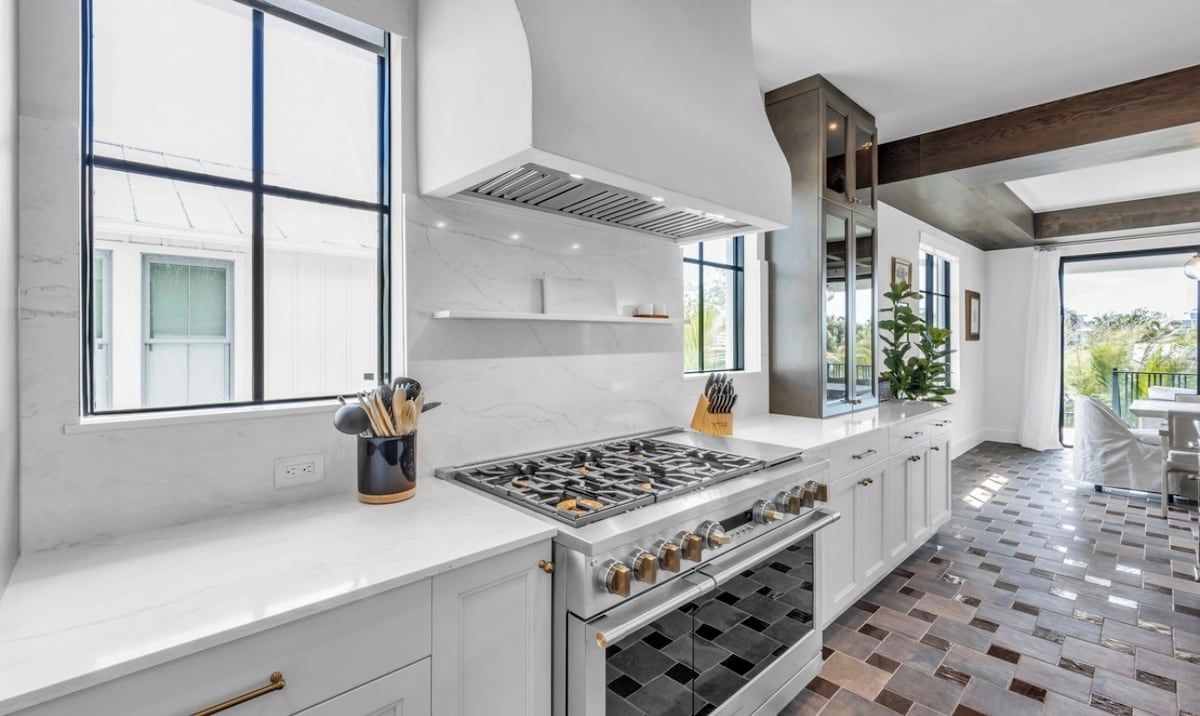 A modern kitchen with a large gas stove, white cabinetry, and a view to the outside.