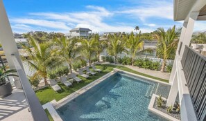 A swimming pool with lounge chairs, surrounded by palm trees and a clear sky. - New Canal Front Beach House on AMI! Gorgeous Pool! (Anna Maria)