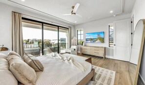 A modern bedroom with a large bed, a TV, a balcony, and a view of the city. - New Canal Front Beach House on AMI! Gorgeous Pool! (Anna Maria)