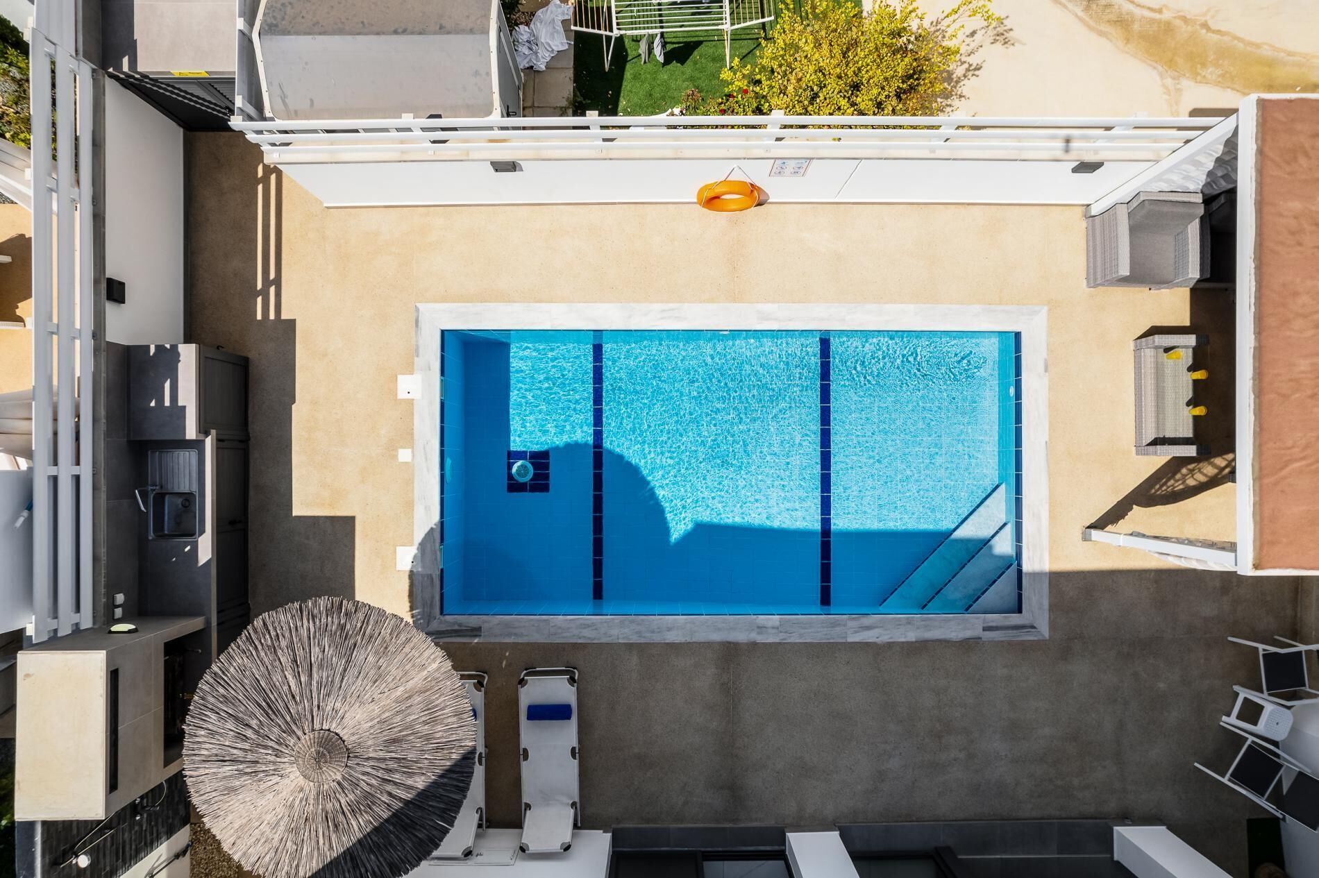 Vue aérienne d’une piscine sur le toit, dont l’eau est d’un bleu limpide, entourée d’un mur beige et d’une rambarde blanche.