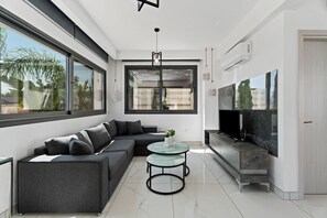 A modern living room with a sectional sofa, a glass coffee table, and a flat-screen TV. - Villa Alassia 16 by Ezoria Villas (Paralimni)