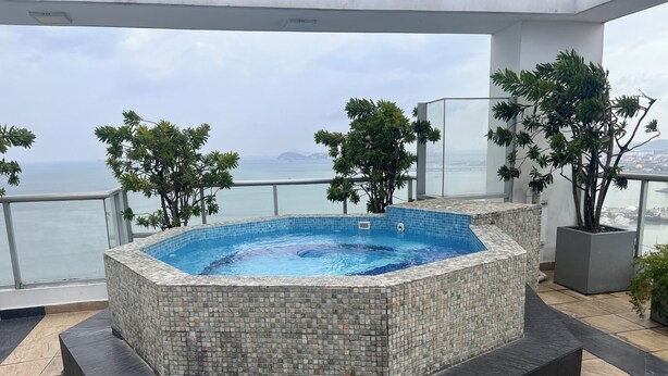 Een hottub met betegelde buitenkant, omringd door potplanten, op een balkon met uitzicht op zee.