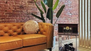 En stue med en murstensvæg, en brun lædersofa, en stor plante og en vintage radio.