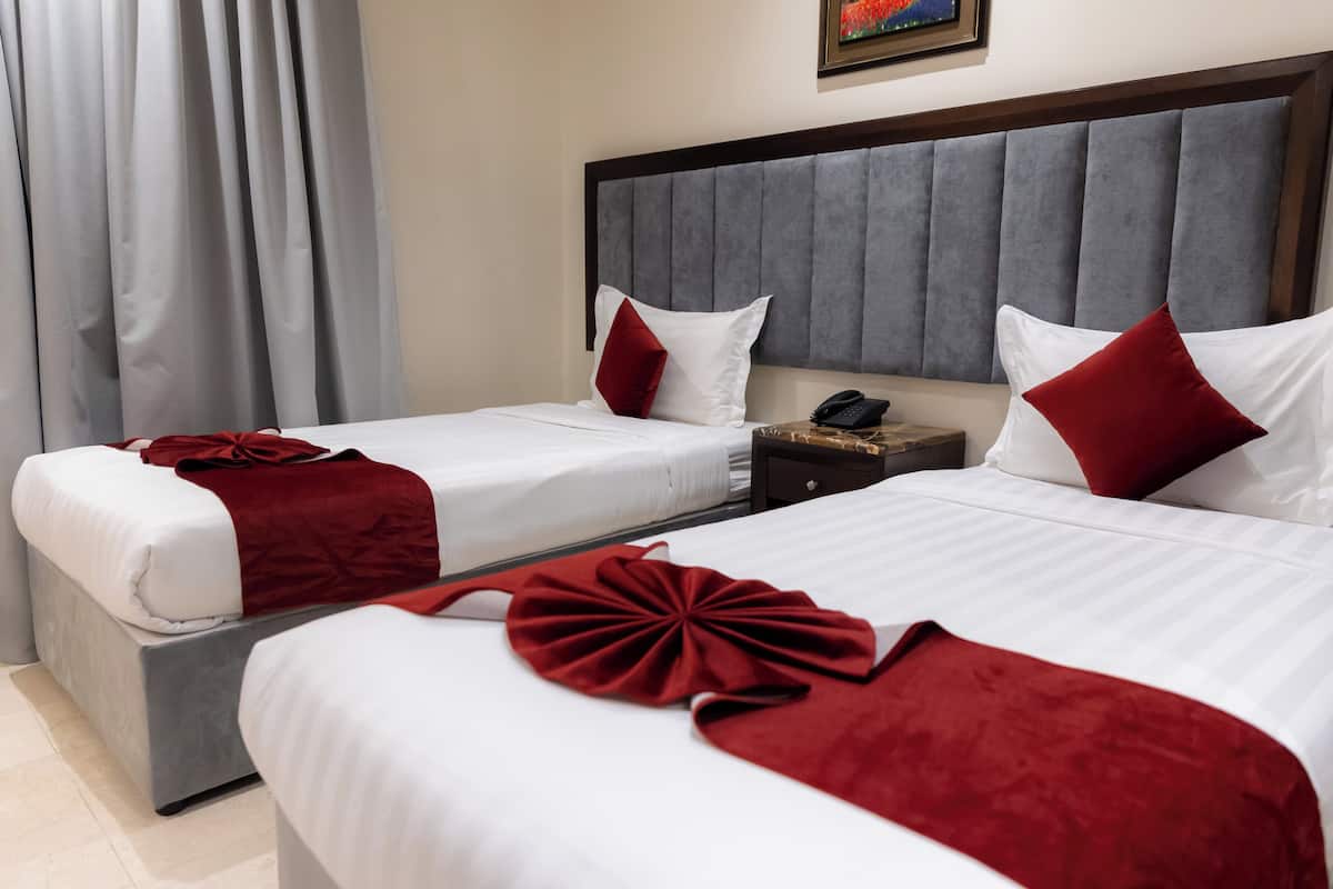 A hotel room with two beds, each with white linens and red accents, a wooden headboard, and a nightstand with a phone.