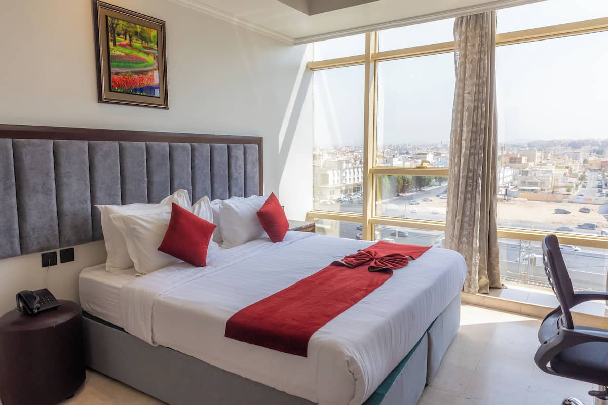 A hotel room with a large bed, a view of the city, and a painting on the wall.