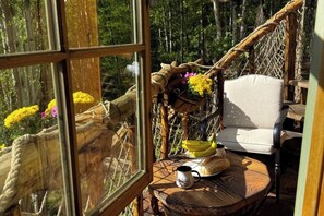 A rustic wooden table with a woven chair, a hammock, and a view of a forest through a large window. - Charming TREEHOUSE in remote location (Braintree)
