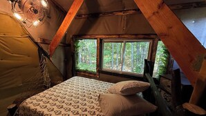 A cozy bedroom with a bed, a window with a view of the forest, and a hanging light fixture. - Charming TREEHOUSE in remote location (Braintree)