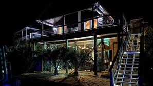 A modern house with a glass facade, a wooden deck, and a staircase leading to a balcony.