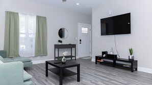 Un salon moderne avec un canapé gris, une table basse noire, un téléviseur fixé au mur et un meuble noir pour appareils multimédias.