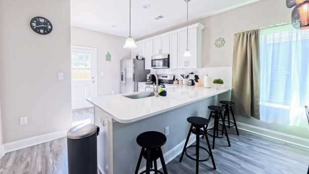 Une cuisine moderne dotée d’un îlot central, de tabourets de bar, d’appareils électroménagers en acier inoxydable et de luminaires suspendus.