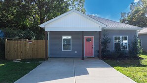 Une petite maison de plain-pied avec une porte rouge, un porche avant couvert et une clôture en bois.
