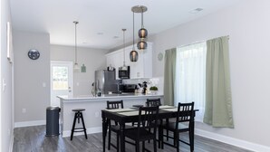 Une cuisine moderne avec des meubles blancs, un réfrigérateur en acier inoxydable et un coin repas comprenant une table et des chaises noires.