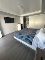 Una habitación de hotel moderna con una cama grande, un televisor de pantalla plana montado en la pared y un vestidor.