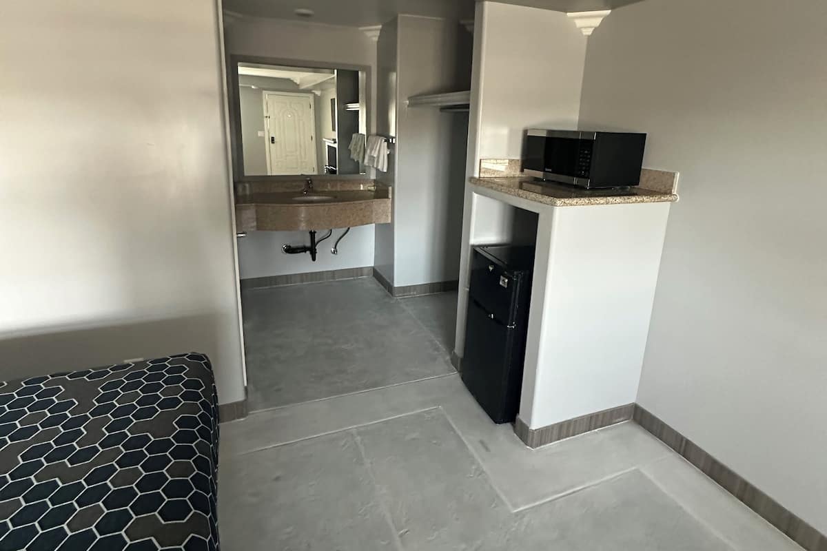 Une chambre d’hôtel compacte, dotée d’une kitchenette, d’un lit recouvert d’une housse à motifs et donnant sur la salle de bain attenante.