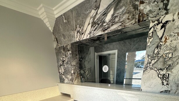 A reception area with marble walls, a reception desk, and a staircase leading to an upper floor. - Hometown Inn (Los Banos)