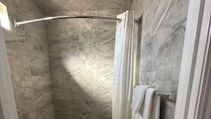 A bathroom with a shower, toilet, and marble walls. - Hometown Inn (Los Banos)
