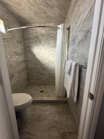 Un baño con ducha, inodoro y paredes de mármol.