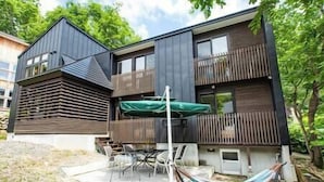 Uma casa moderna de dois andares, com varanda, um alpendre com mobiliário de exterior e uma rede.
