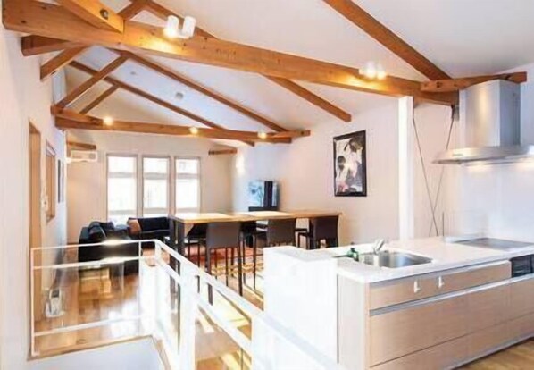 A modern kitchen with wooden beams, a dining area, and a staircase.