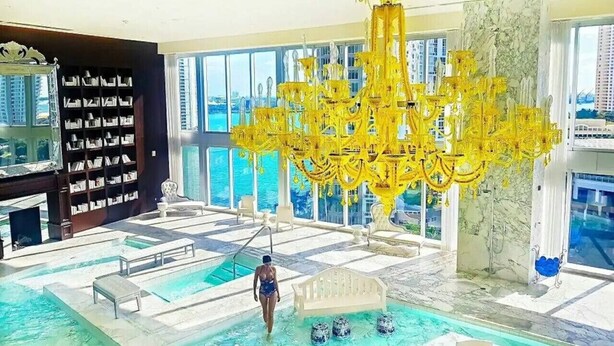 Une vaste piscine intérieure, agrémentée d’un grand lustre jaune, d’un banc blanc et d’une bibliothèque remplie de livres.