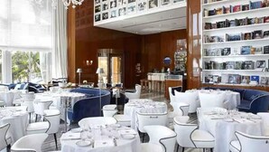 Un restaurant avec des tables rondes, des chaises blanches et un canapé bleu.